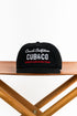 Black cap with white and red text on a wooden stand against a white background